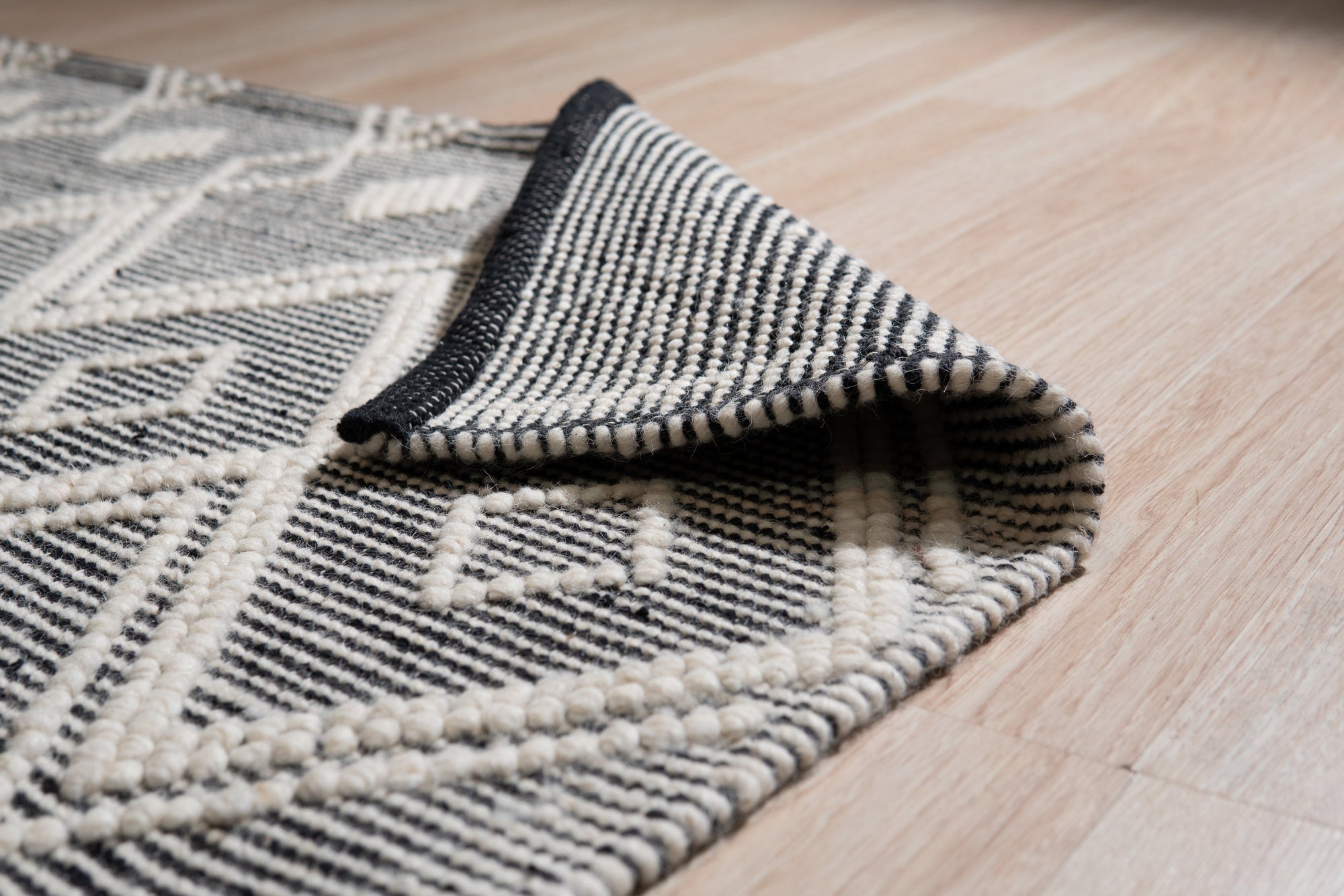 Modern Kilim Black Handmade Wool Rug, showcasing a geometric pattern in contrasting shades of black and off-white, lies flat on a light-colored floor, suggesting a modern living space.