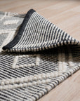 Modern Kilim Black Handmade Wool Rug, showcasing a geometric pattern in contrasting shades of black and off-white, lies flat on a light-colored floor, suggesting a modern living space.