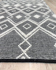 Luna Kilim Black Handmade Wool Rug draped across a light grey sofa, showcasing its geometric pattern and textural weave against the backdrop of a bright, modern living room.