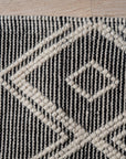 Luna Kilim Black Handmade Wool Rug displayed in a bright, modern living room. Woven black wool rug with geometric kilim patterns grounds a seating area with a light sofa and minimalist decor.