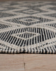Luna Kilim Black Handmade Wool Rug, woven geometric patterns dance across a black wool field, grounding a modern living room with hardwood floors and bright, natural light.