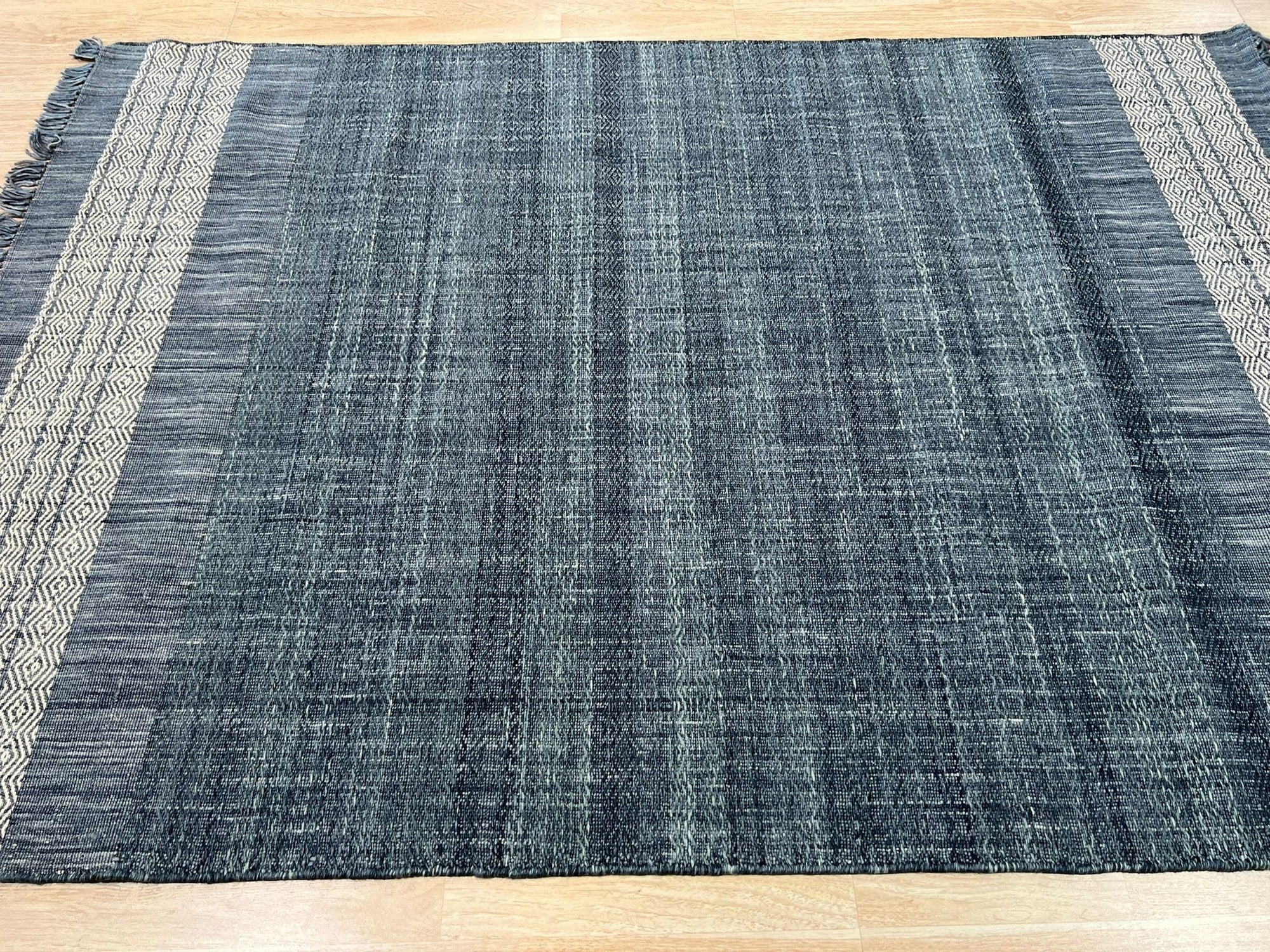 Delicate Elena Blue Flatweave Wool Rug, a soft blue wool rug with a subtle geometric pattern, lies flat on a light wood floor, subtly textured and inviting.