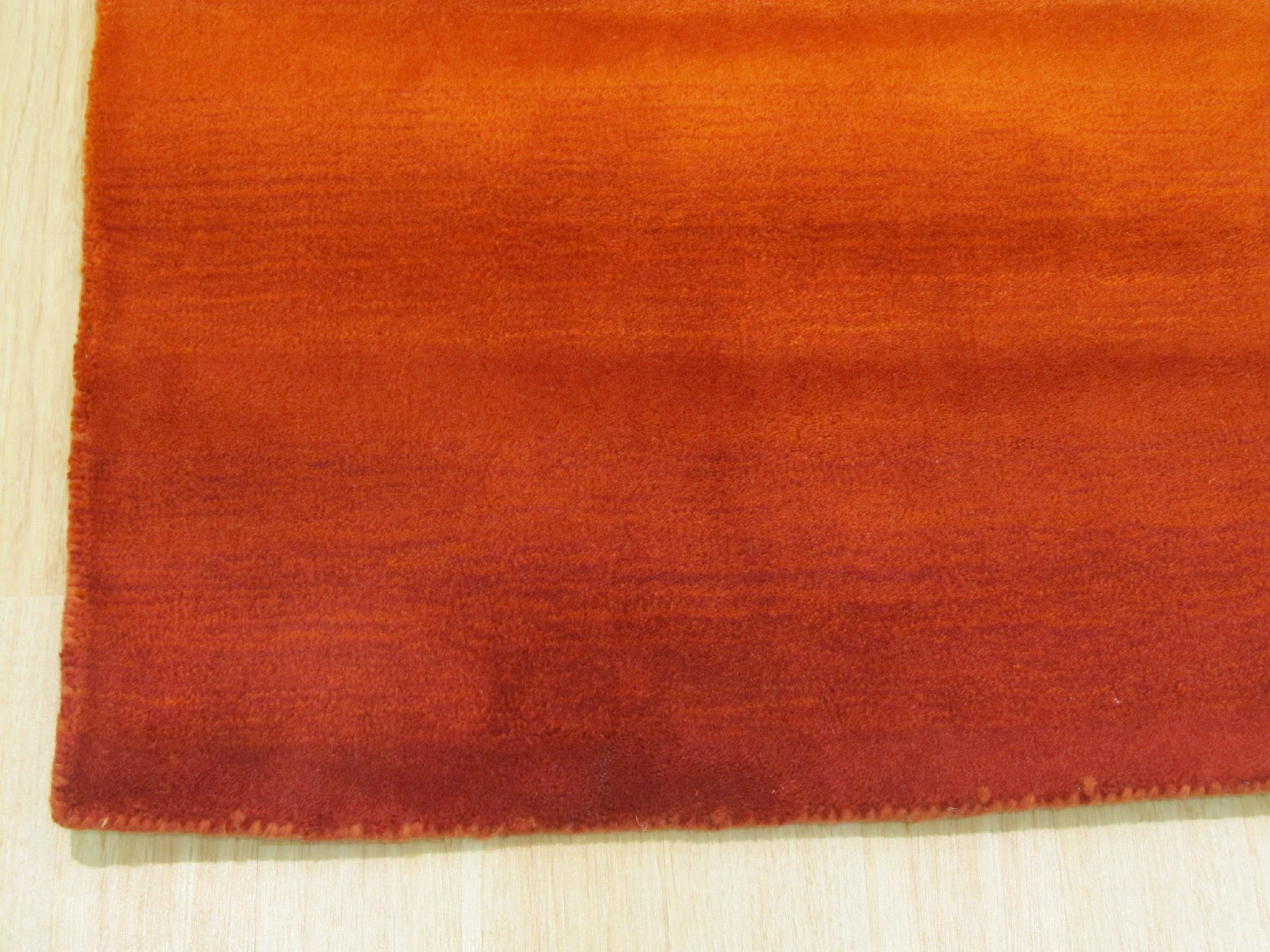 Ruby Classic Orange Handmade Wool Rug, showing detailed texture and vibrant orange hues, lies partially beneath a dark wood coffee table with a golden base, blending traditional design with modern decor in a warmly lit living room setting.