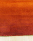 Ruby Classic Orange Handmade Wool Rug, showing detailed texture and vibrant orange hues, lies partially beneath a dark wood coffee table with a golden base, blending traditional design with modern decor in a warmly lit living room setting.