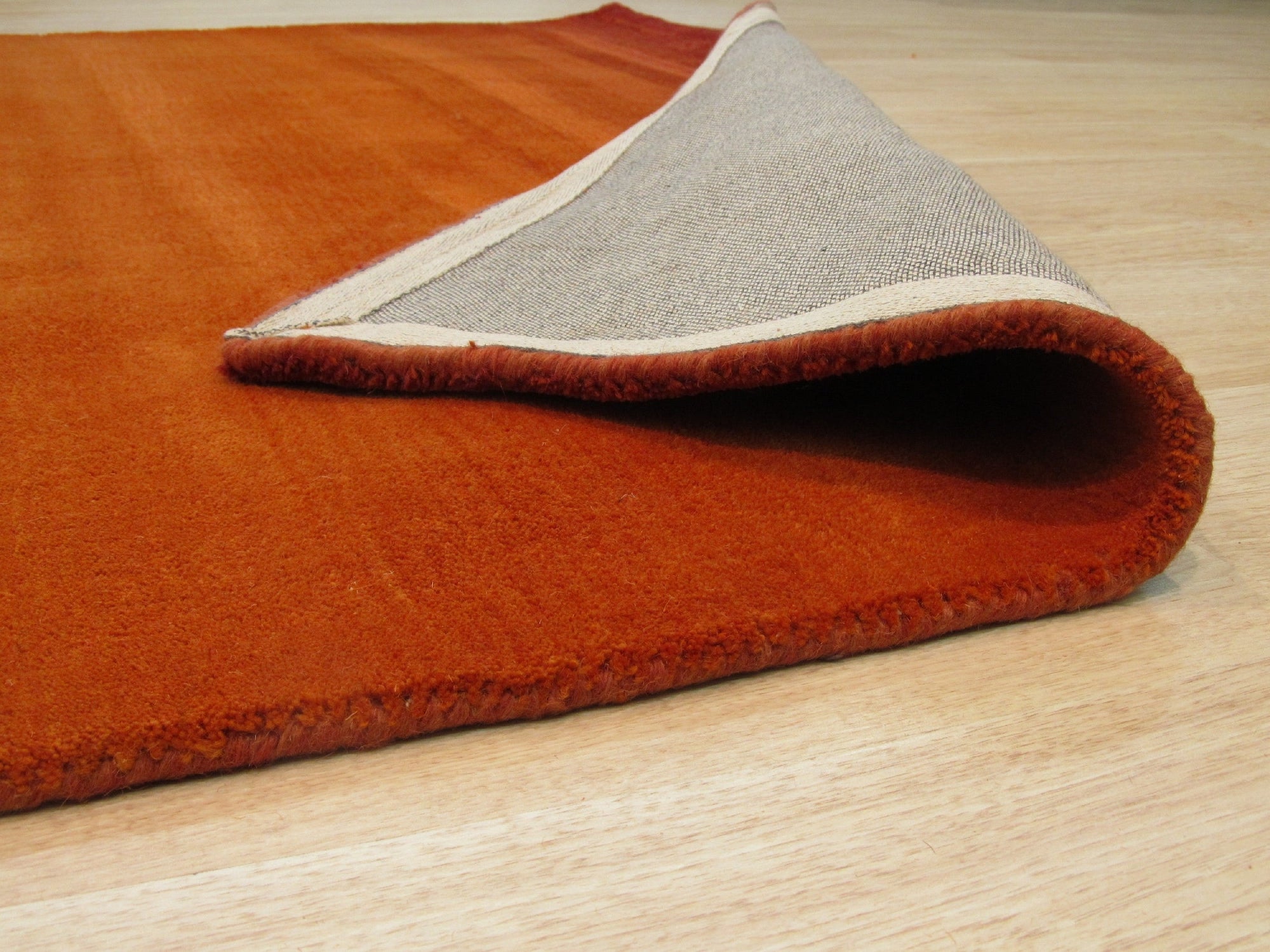 Ruby Classic Orange Handmade Wool Rug displaying warm, earthy tones and intricate patterns under soft lighting, highlighting its handcrafted texture and vibrant color palette.