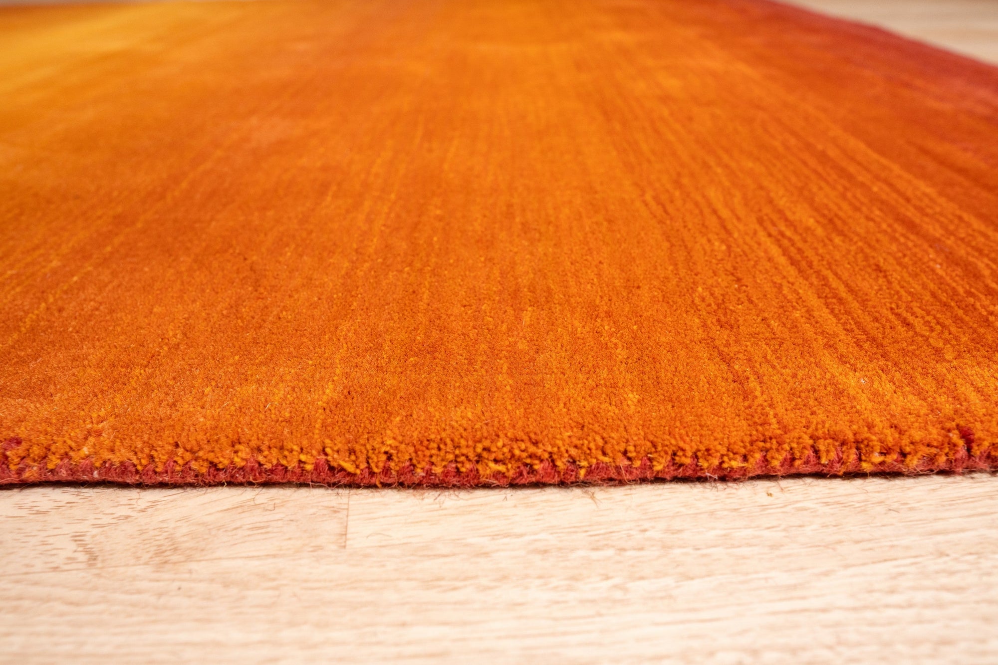 Ruby Classic Orange Handmade Wool Rug, showcasing vibrant orange hues and intricate patterns, laying in a brightly lit living room setting.