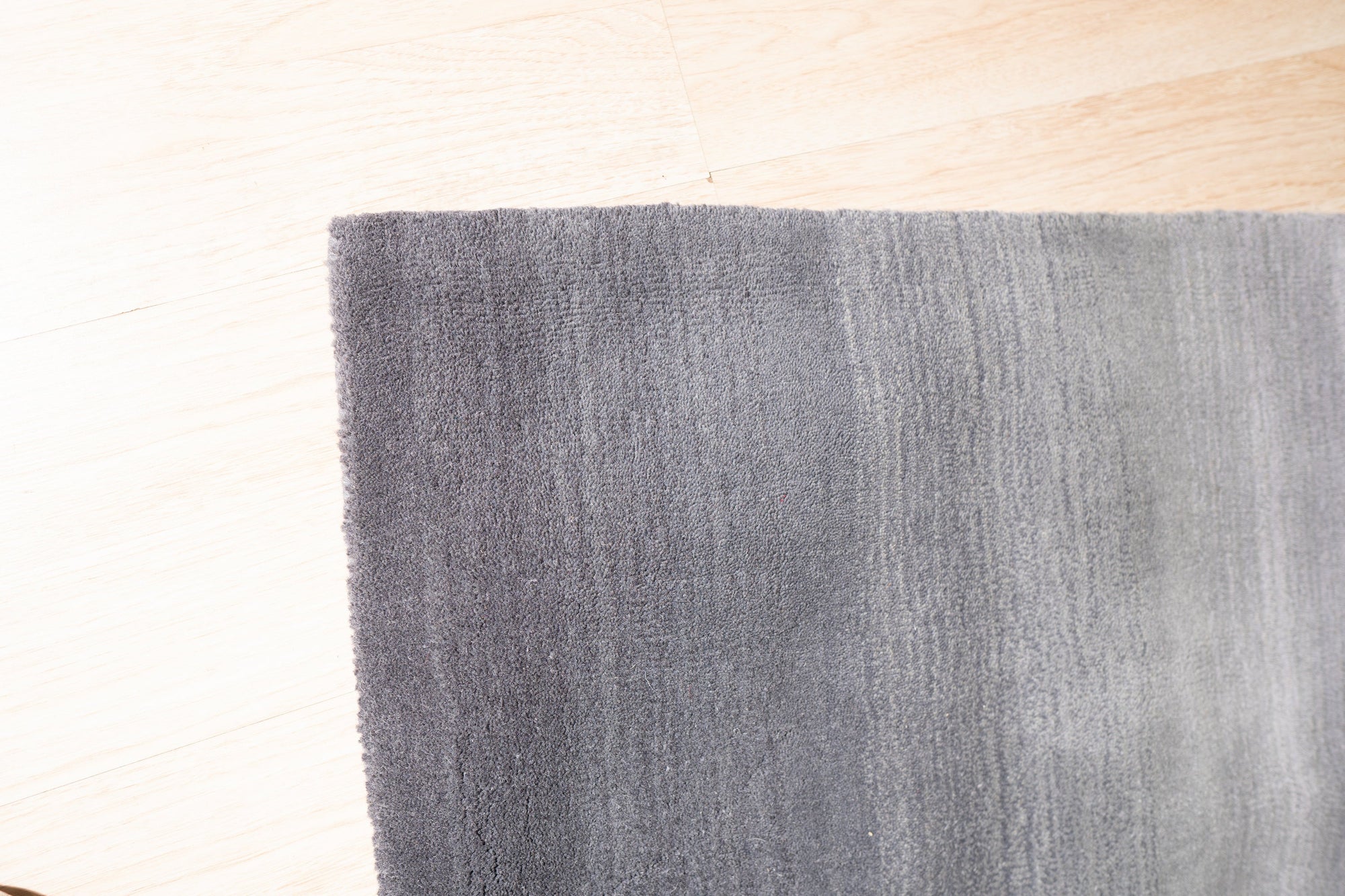 Modern Talia Gray Handmade Wool Rug, showcasing subtle geometric patterns in varying shades of gray, lies on a light hardwood floor in a bright living space; neutral furniture complements the rug's calming color palette.