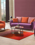 Rhea Unique Multicolor Handmade Wool Rug, filling a modern living space with vibrant, geometric patterns in shades of blue, orange, and cream. Light wood floors and a minimalist sofa complement the rug's bold design.