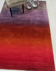 Rhea Unique Multicolor Handmade Wool Rug, sprawling across hardwood flooring, its vibrant hues of teal, gold, and coral interweaving in a captivating abstract pattern, a corner gently hinting at a nearby sofa.