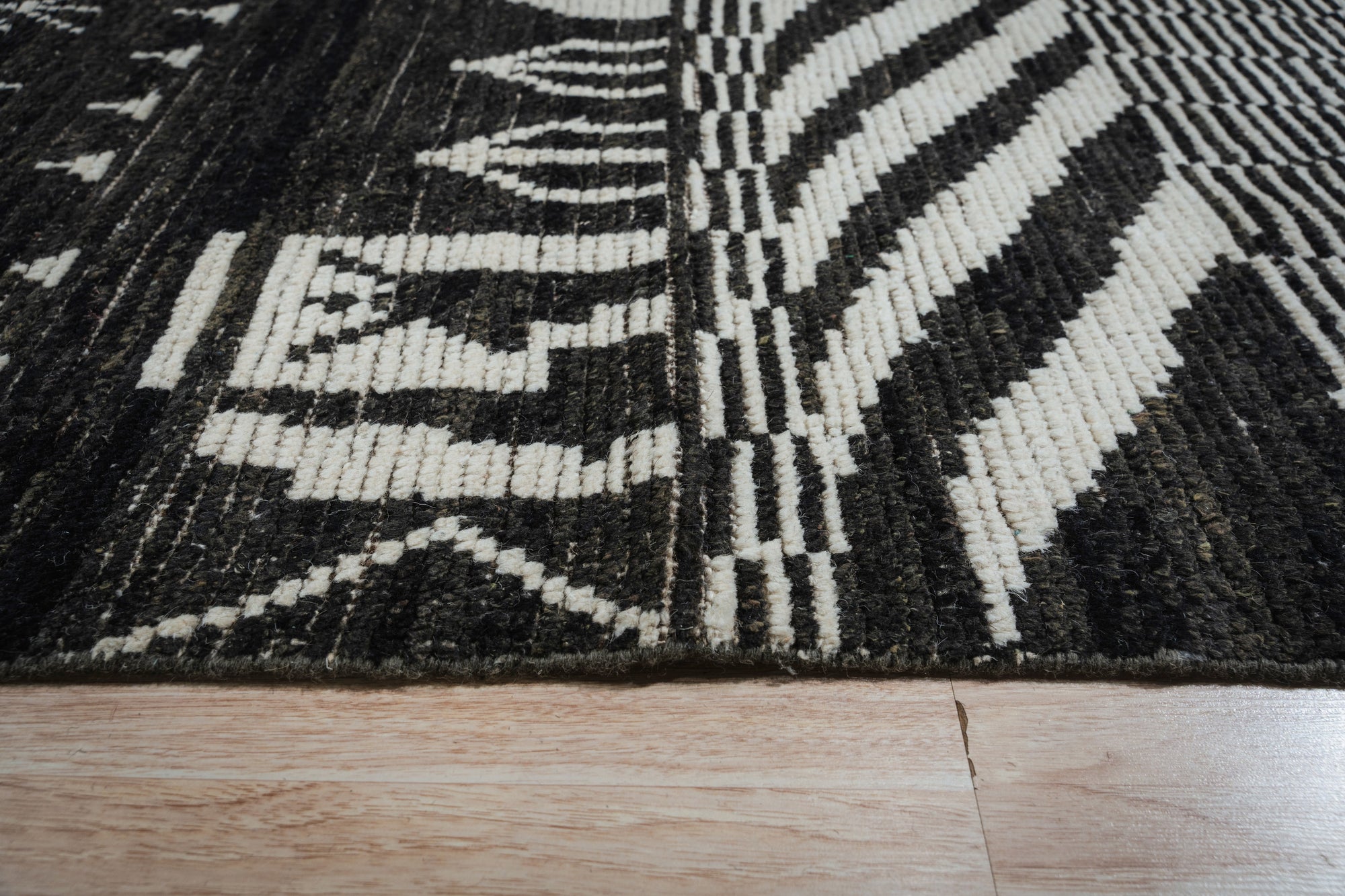 Marrakech Essence Black Rug gracing a stylish living room. Woven threads create a textured surface, the black backdrop accented with a subtle, modern pattern hinting at Moroccan influences.