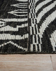 Marrakech Essence Black Rug gracing a stylish living room. Woven threads create a textured surface, the black backdrop accented with a subtle, modern pattern hinting at Moroccan influences.
