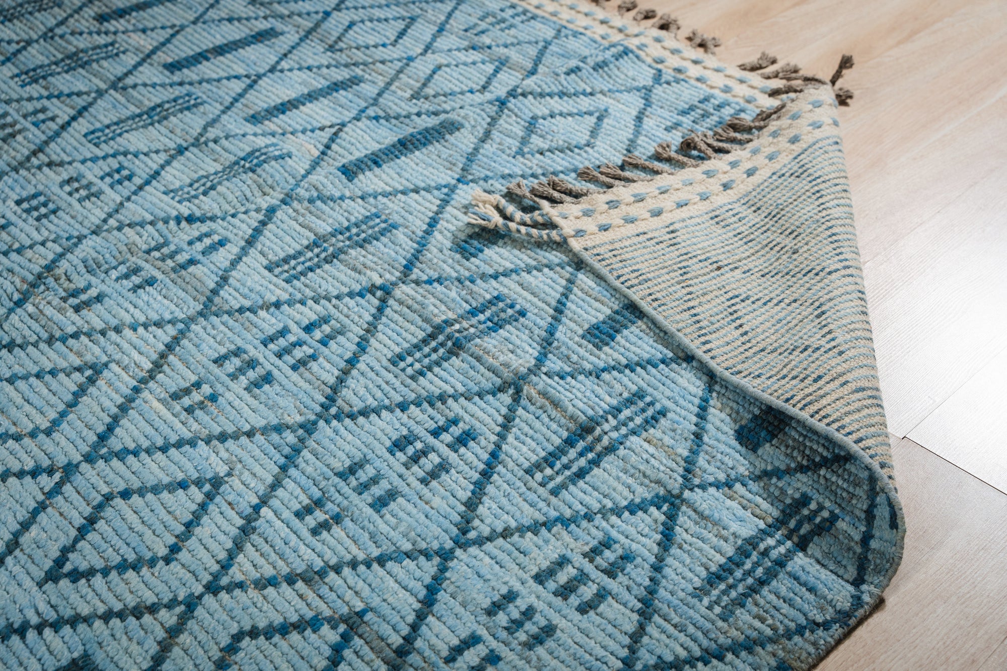 Stylish Marrakech Blue Hand-Knotted Wool Rug gracing a light wood floor, its intricate geometric pattern in shades of blue and cream providing a vibrant yet calming foundation for a modern living space.
