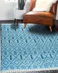 Stylish Marrakech Blue Hand-Knotted Wool Rug, its vibrant blue and cream geometric pattern grounding a contemporary living space with a dark wood coffee table and light gray sofa.