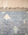 Charming Marrakech Blue Hand-Knotted Wool Rug, showcasing intricate geometric patterns in shades of blue and cream, adding warmth and texture to a warmly lit living room.