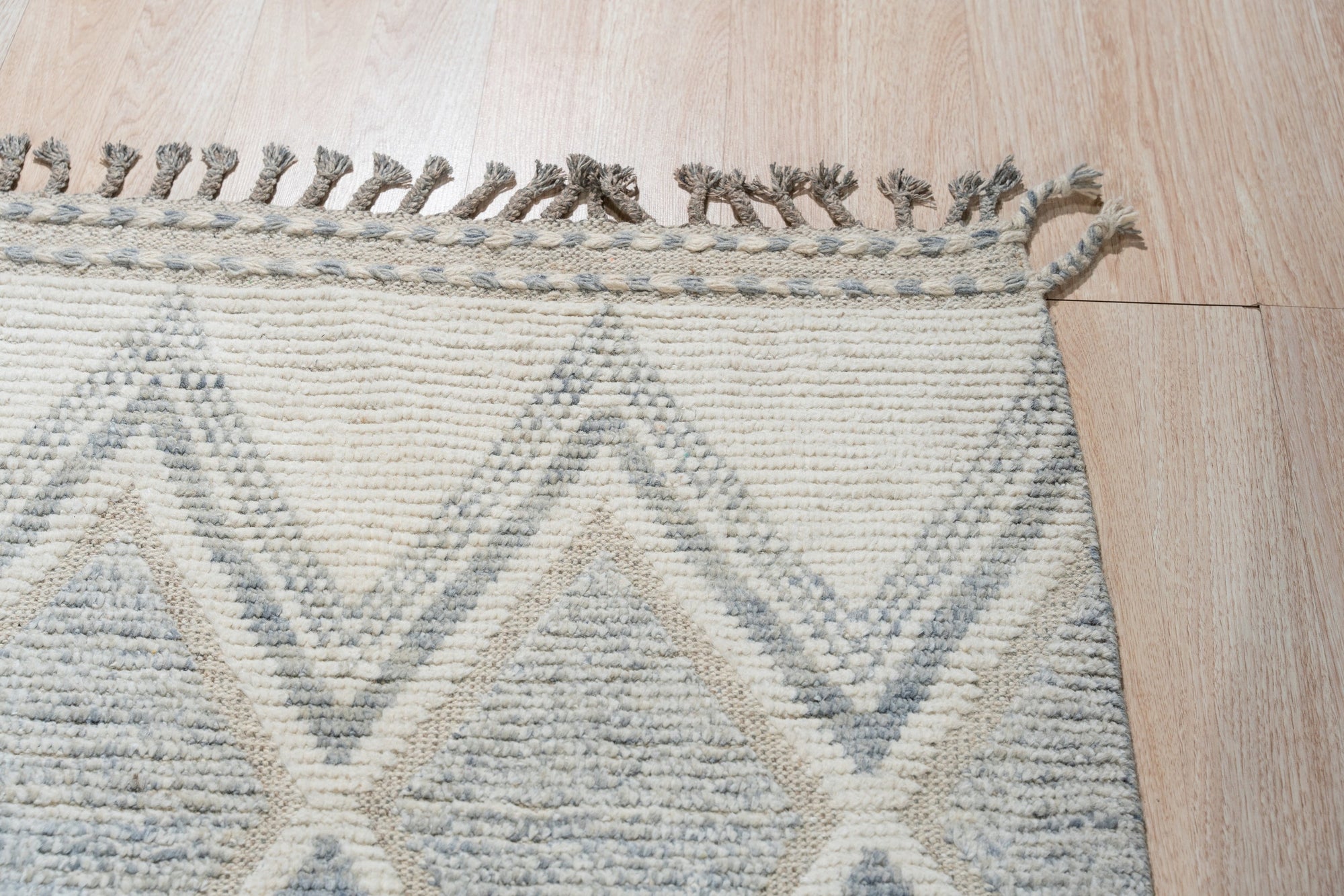 Elegant Marrakech Beige Hand-Knotted Wool Rug, showcasing intricate geometric patterns in muted beige tones, laid against a warmly lit wooden floor.