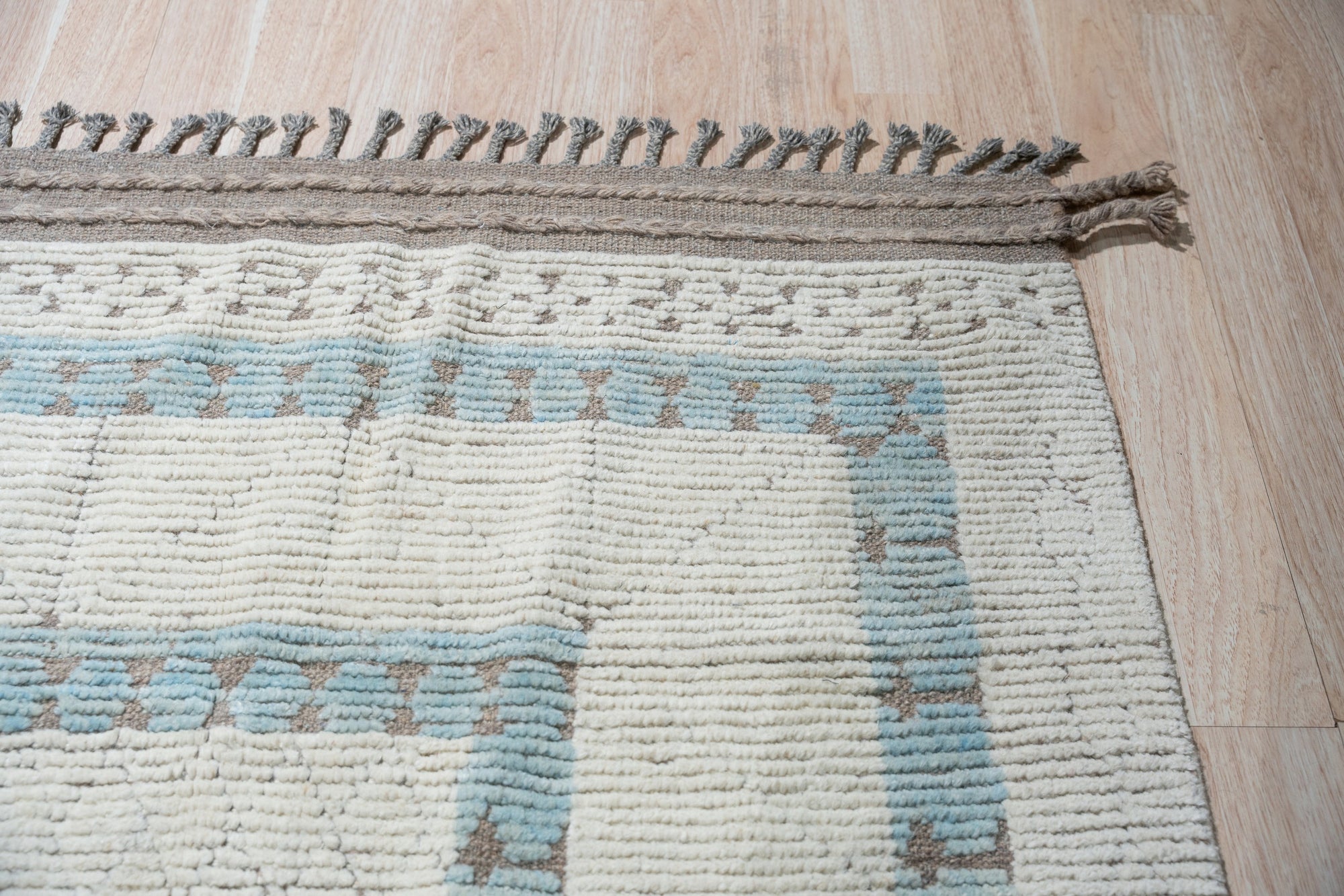 Timeless Marrakech Beige Hand-Knotted Wool Rug, textured wool underfoot with a classic Moroccan-inspired pattern, anchors a bright living space featuring a light wood coffee table and modern seating.