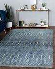 Refined Marrakech Blue Hand-Knotted Wool Rug, with intricate geometric patterns in varying shades of blue and cream, laid on a dark hardwood floor creating a cozy, inviting atmosphere.