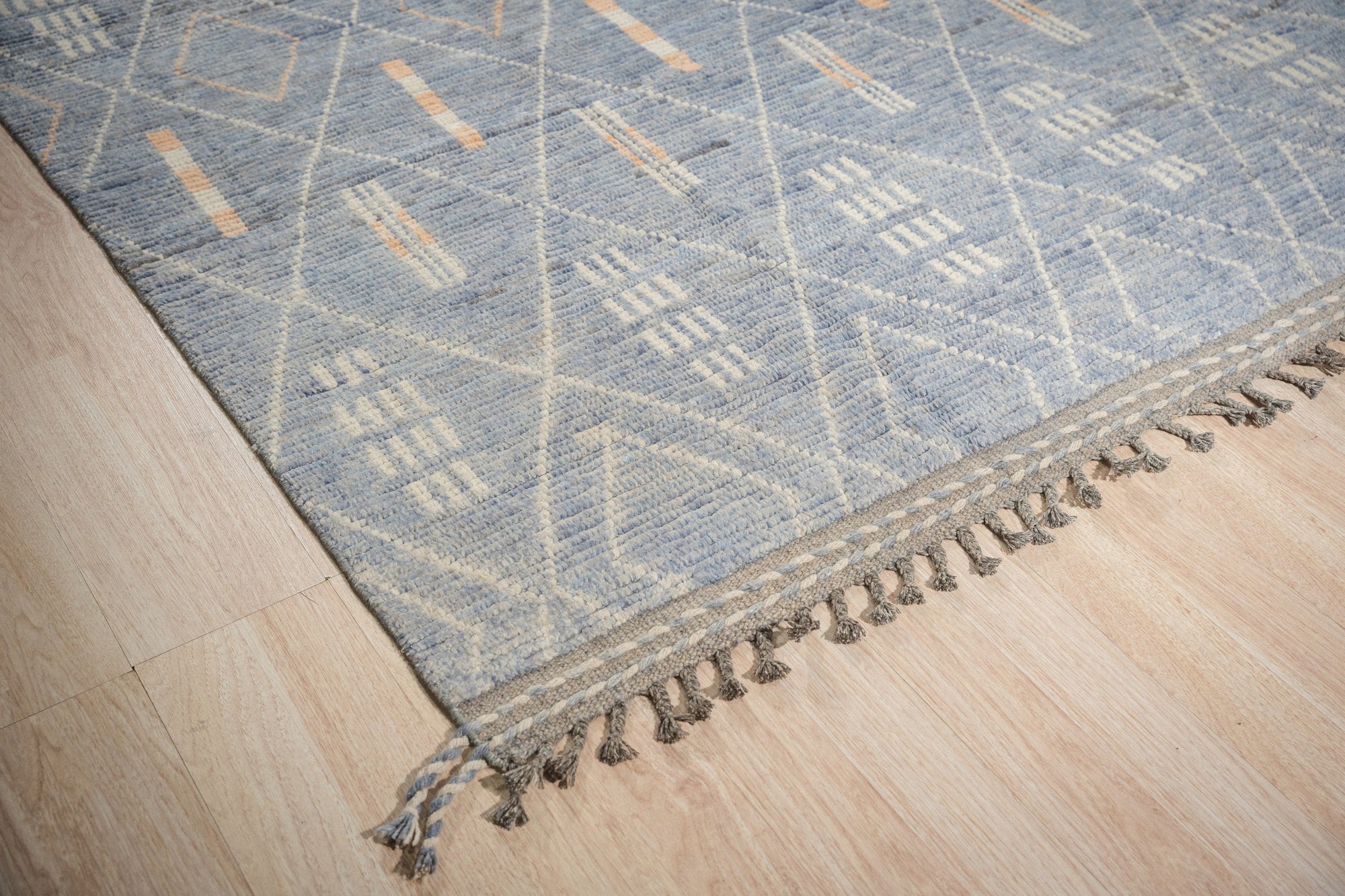 Graceful Marrakech Blue Hand-Knotted Wool Rug, its intricate geometric pattern in shades of blue and cream, sprawls across a light wood floor, creating a warm and inviting ambiance.