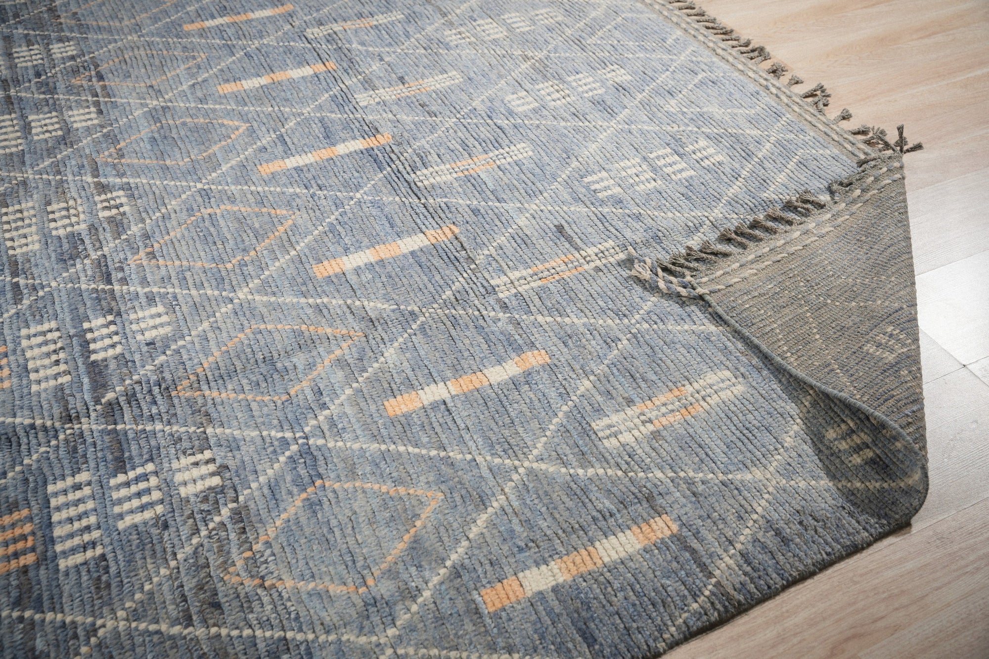 Graceful Marrakech Blue Hand-Knotted Wool Rug, displaying intricate geometric patterns in shades of blue and ivory, resting on a polished hardwood floor in a well-lit room.
