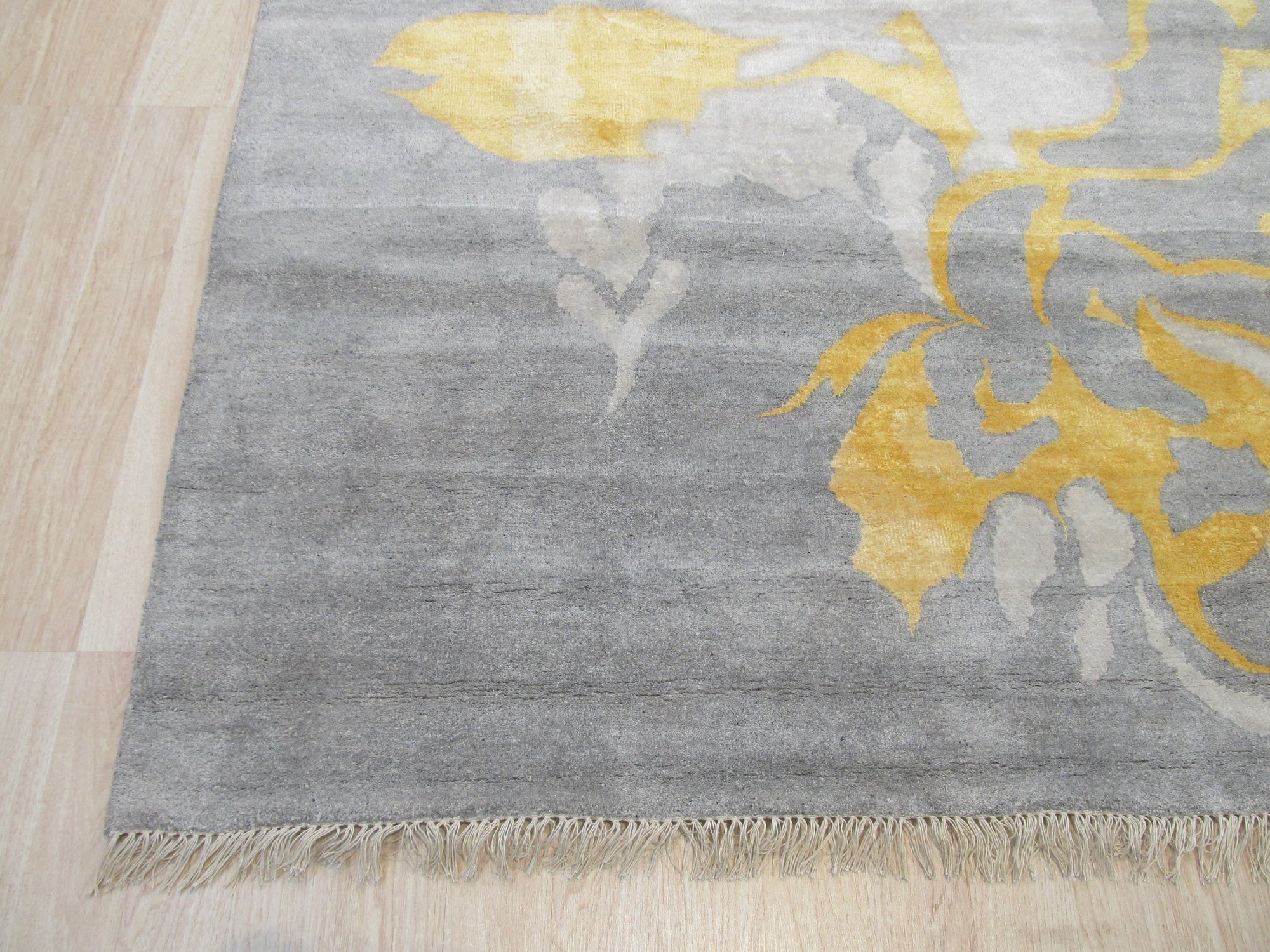 Sloane Giselle Gray Hand Knotted Wool & Viscose Rug displayed in a bright living room setting. Warm sunlight illuminates the rug's soft grey tones and subtle texture, highlighting its hand-knotted construction.