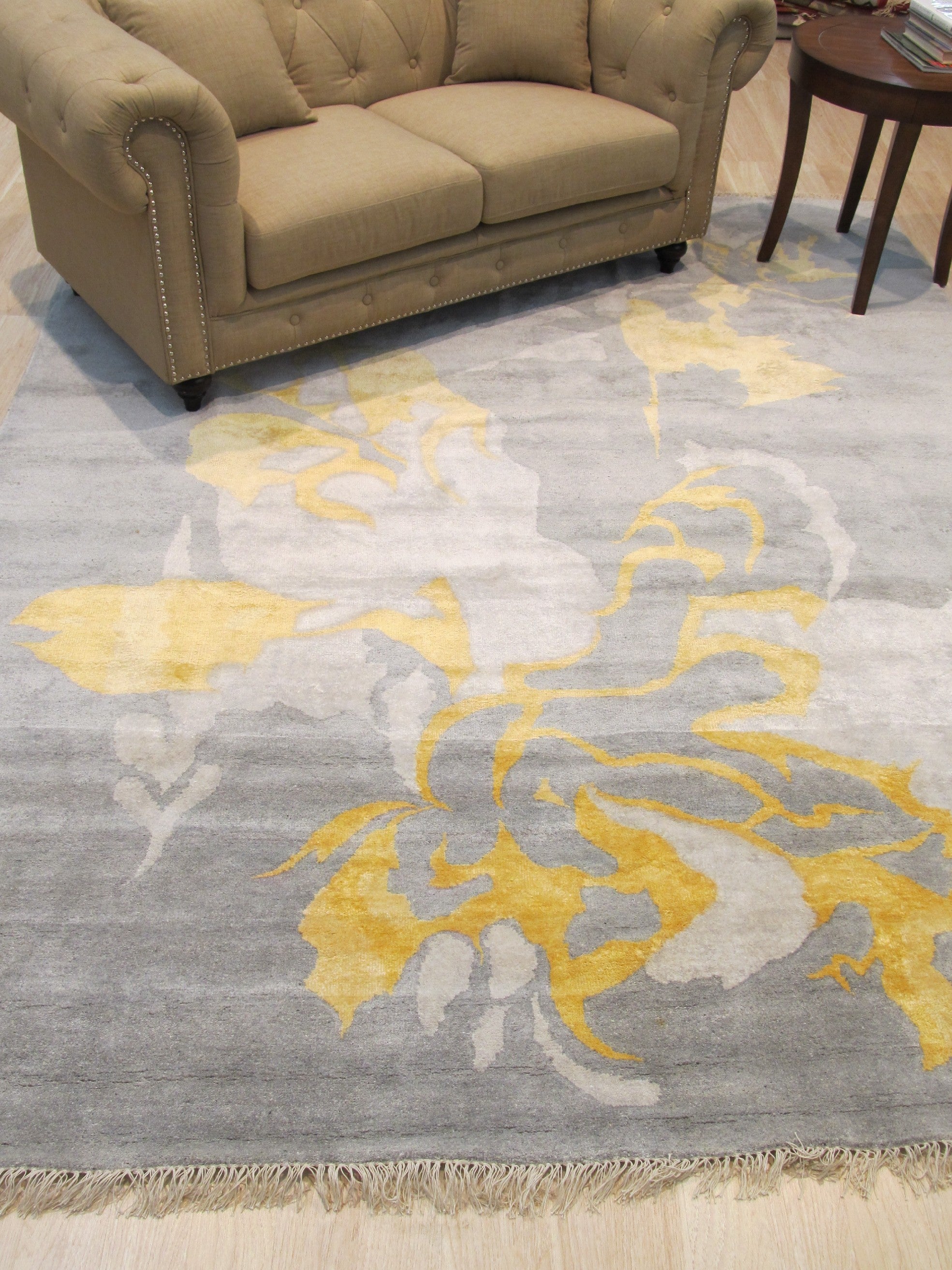 Sloane Giselle Gray Hand Knotted Wool & Viscose Rug, a luxurious blend of wool and viscose, rests on a dark wood floor, its subtle gray tones and intricate hand-knotted design creating a sophisticated and calming atmosphere within a softly lit room.