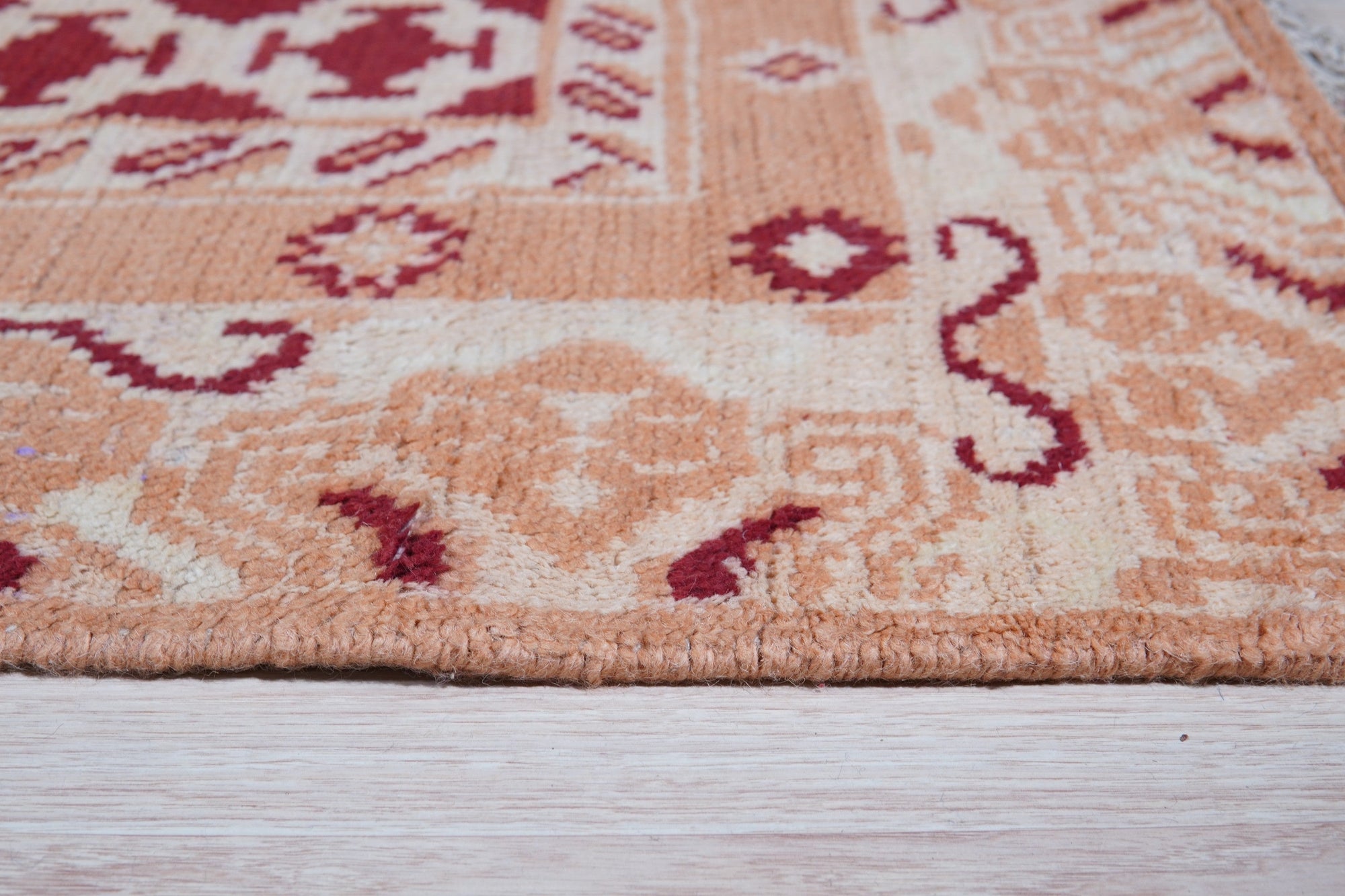 Chloe Trara Red Hand Knotted Wool Rug, showcasing intricate patterns woven in rich red tones, lies gracefully on a light hardwood floor, its luxurious texture inviting touch.