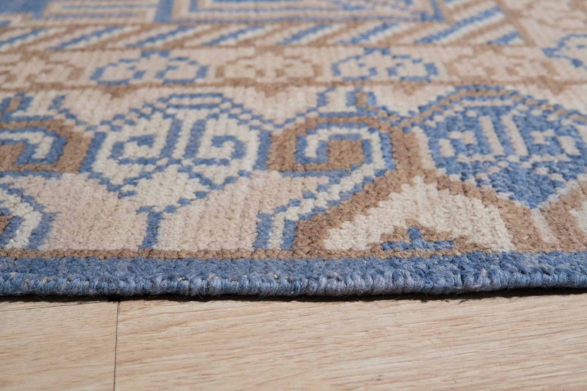 Handcrafted Traditional Blue Hand Knotted Wool Rug, showcasing intricate knotwork and deep blue hues, lies subtly on a light wooden floor, complementing a warmly lit interior.