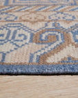 Handcrafted Traditional Blue Hand Knotted Wool Rug, showcasing intricate knotwork and deep blue hues, lies subtly on a light wooden floor, complementing a warmly lit interior.