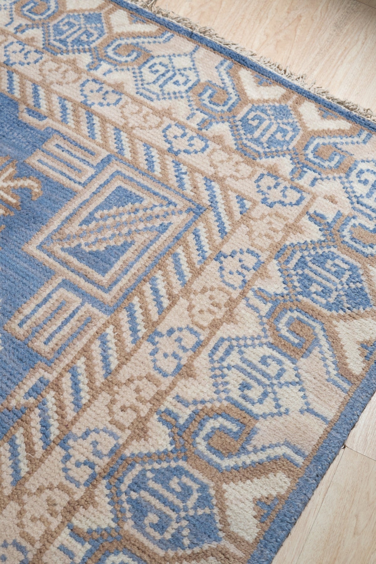 Handcrafted Traditional Blue Hand Knotted Wool Rug, richly patterned with classic motifs in deep blues and subtle creams, lies elegantly on a polished floor, hinting at warmth and timeless style within a softly lit room.