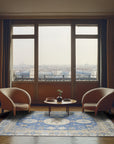 Handcrafted Traditional Blue Hand Knotted Wool Rug, featuring intricate geometric patterns in shades of blue and cream, displayed in a brightly lit living room setting.