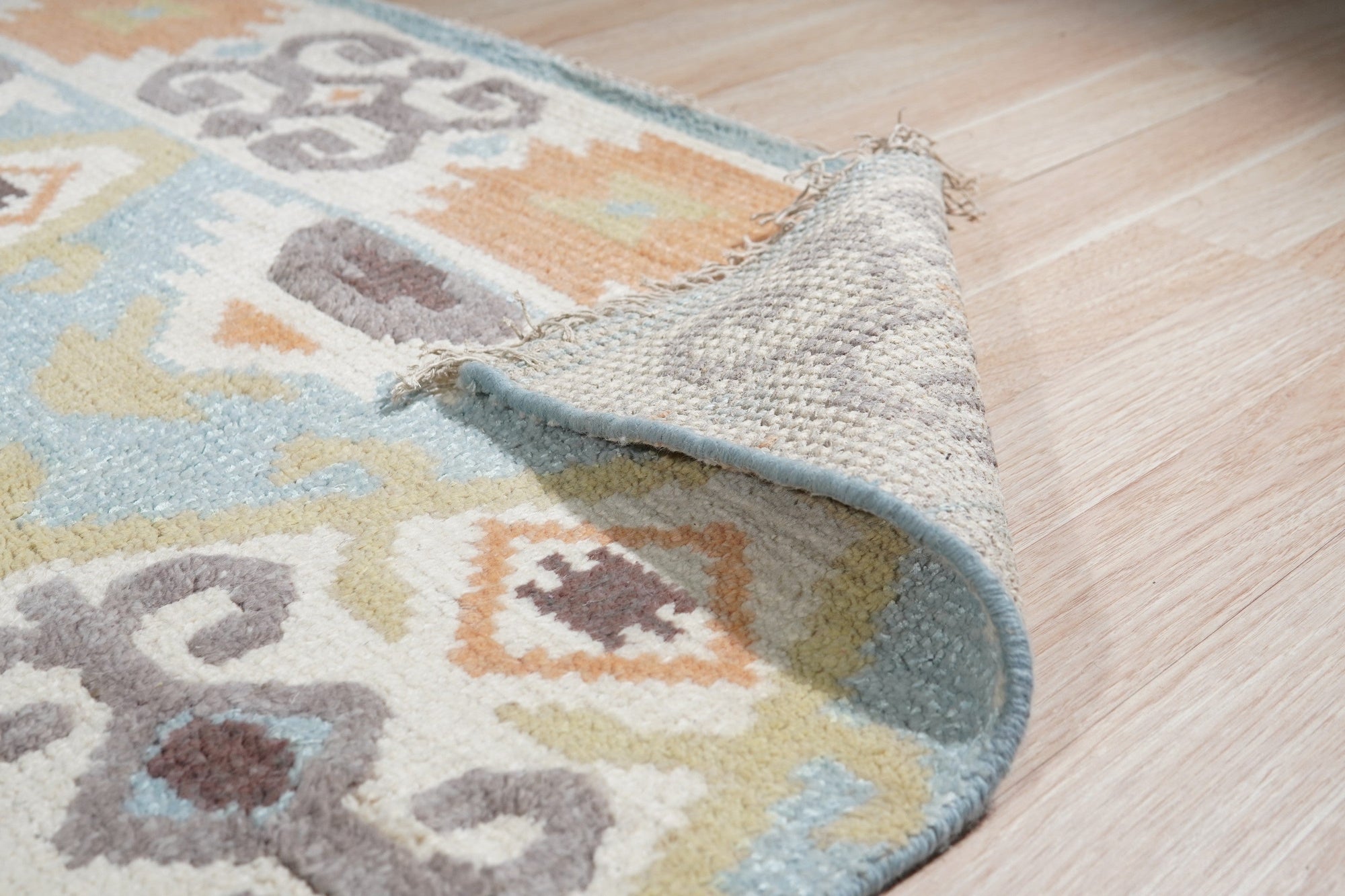 Freya Traditional Blue Hand Knotted Wool Rug, showcasing intricate floral and geometric patterns in shades of blue, cream, and beige, rests on a dark hardwood floor with natural light highlighting its soft texture.