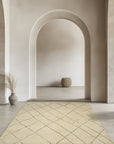 Jade Trellis Beige Hand Knotted Wool Rug, a soft beige wool rug featuring a repeating trellis pattern, warmly anchors a well-lit living space with neutral furnishings.