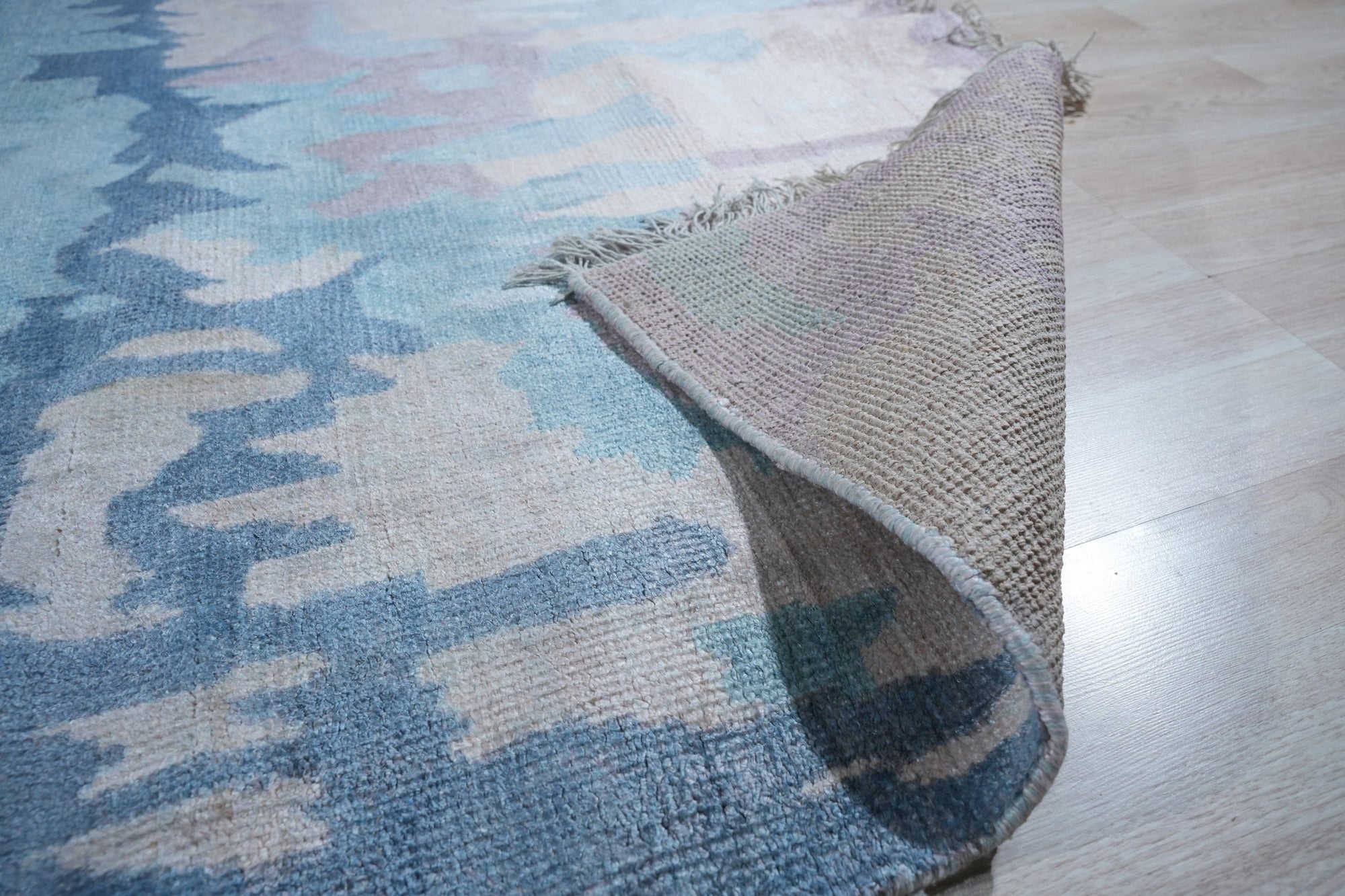 Iris Bianca Multicolor Hand Knotted Bamboo Silk Rug, shimmering with blended hues, sprawls across a light hardwood floor, its intricate design suggesting a blossoming iris rendered in luxurious, silky texture.