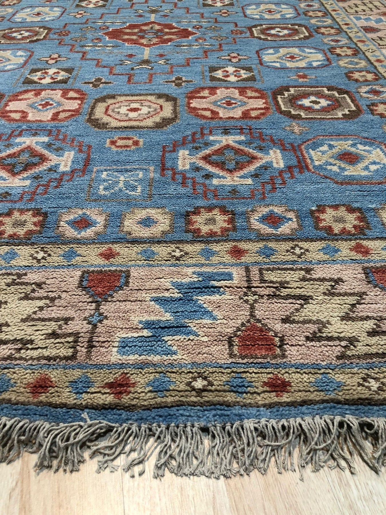 Charming Refined Blue Hand Knotted Wool Rug, its intricate pattern a blend of traditional and modern aesthetics, lies on a polished hardwood floor, casting subtle shadows that highlight its luxurious texture.