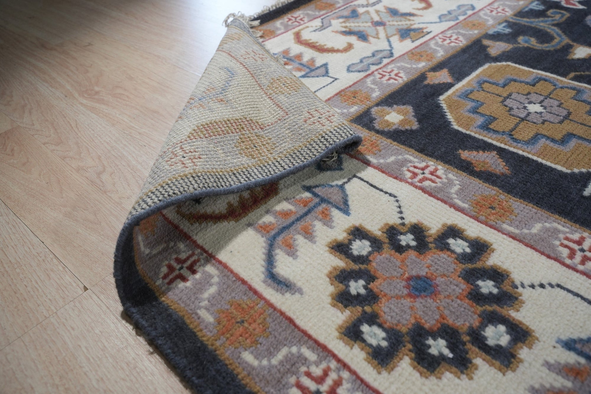 Refined Oushak Charcoal Hand Knotted Wool Rug, charcoal-toned wool rug with a traditional Oushak design, displayed on a light hardwood floor, offering a glimpse of its texture and scale within a room setting.