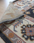 Refined Oushak Charcoal Hand Knotted Wool Rug, charcoal-toned wool rug with a traditional Oushak design, displayed on a light hardwood floor, offering a glimpse of its texture and scale within a room setting.