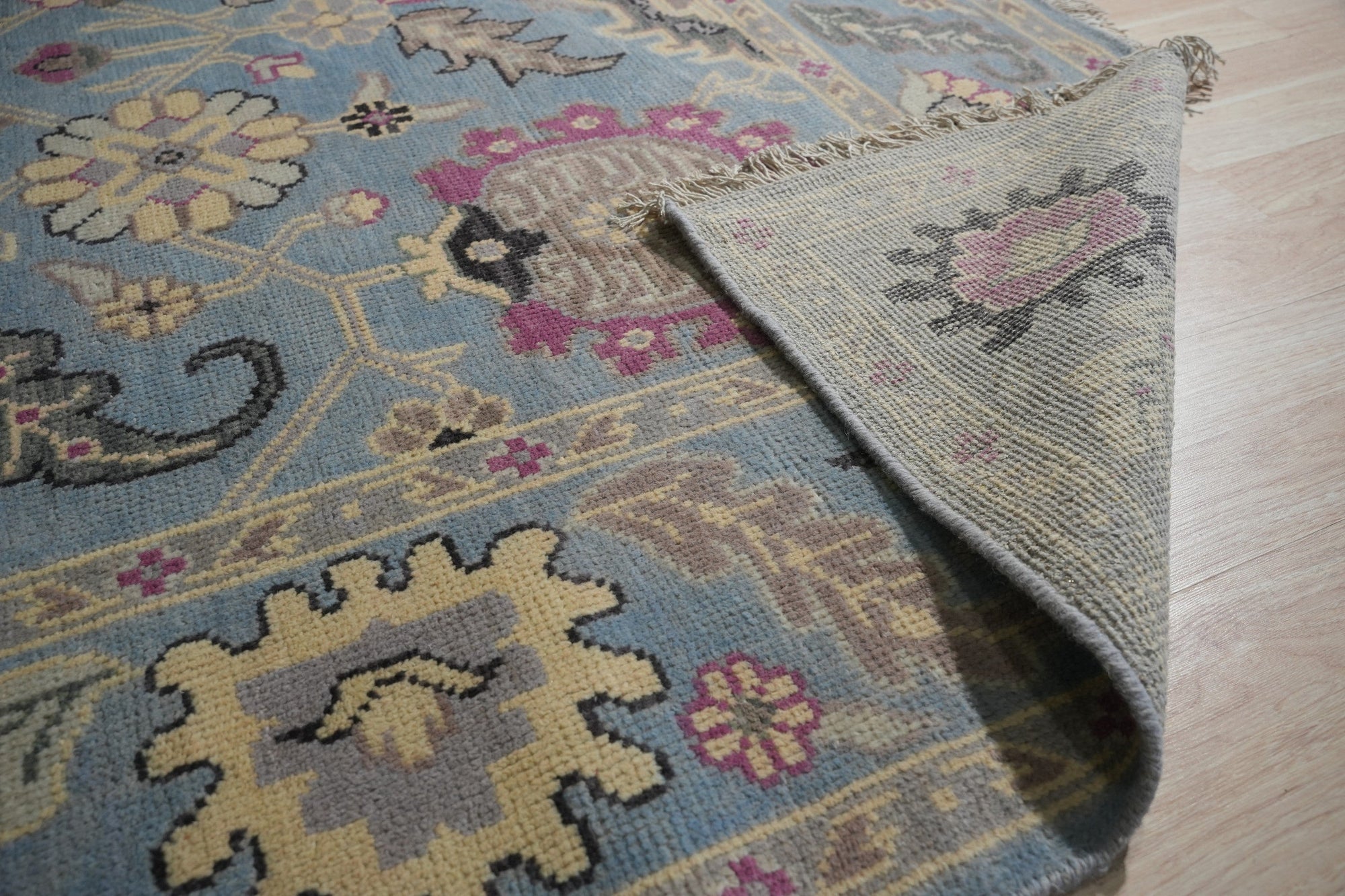 Tessa Laine Blue Hand Knotted Wool Rug, showcasing intricate patterns in varying shades of blue, laid in a bright, naturally lit room with modern furniture. Soft textures and hand-knotted construction visible.