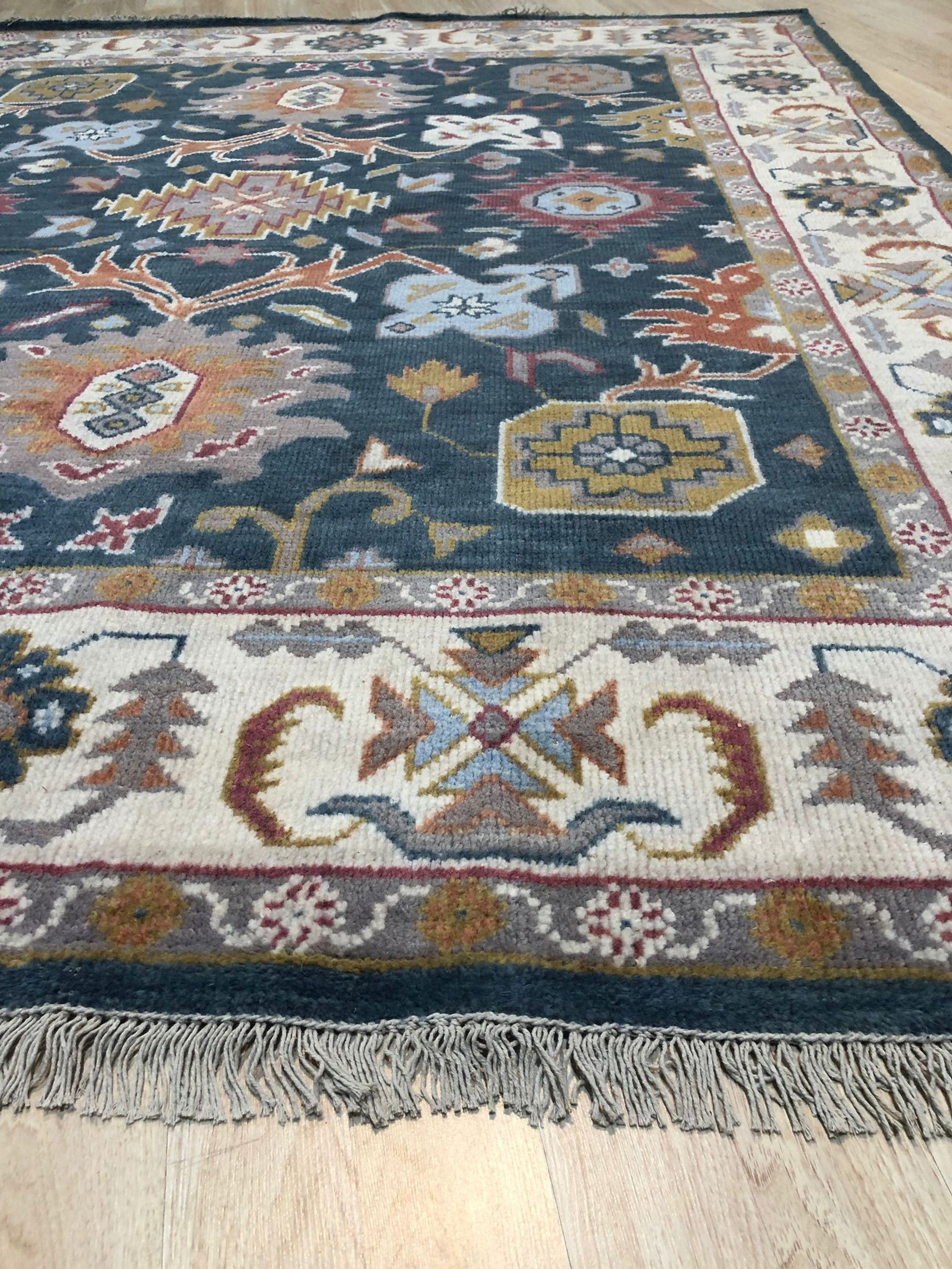 Sarrah Oushak Charcoal Hand Knotted Wool Rug, charcoal wool rug with a traditional Oushak design, seen in a bright, modern living room setting with light wood floors and neutral furniture.