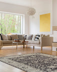 Cozy Oushak Charcoal Hand Knotted Wool Rug, a charcoal wool rug with a traditional Oushak design, seen in a bright, modern living room setting, partially underneath a light-colored sofa and coffee table.