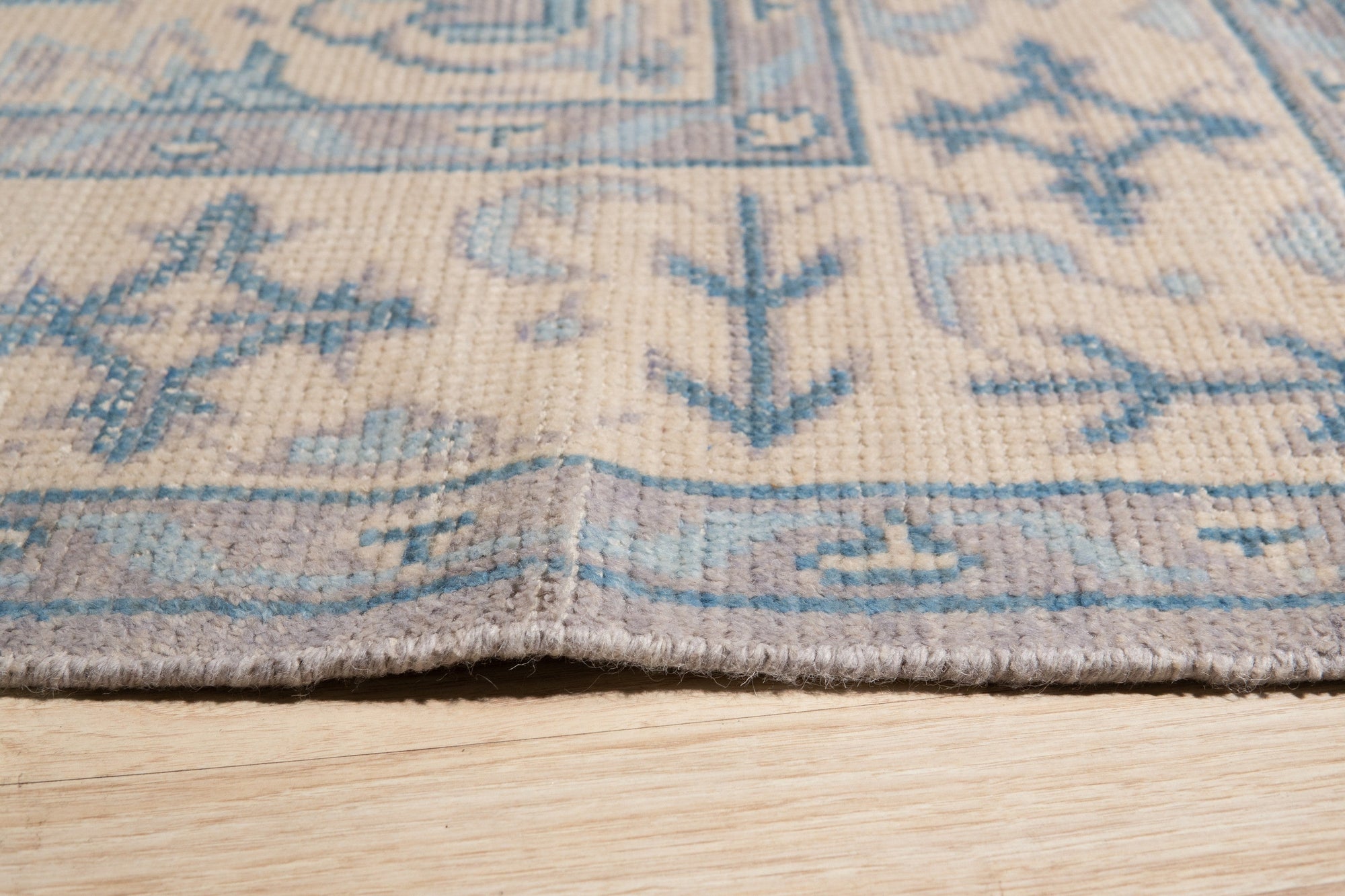 Iris Bianca Gray Hand Knotted Wool Rug, displaying subtle textural variations and a soft, muted gray palette, rests elegantly on a light wood floor. Delicate details and hand-knotted construction are visible in the close-up shot.