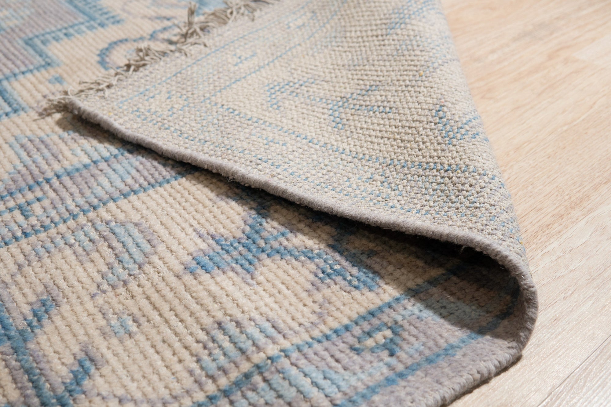Iris Bianca Gray Hand Knotted Wool Rug, featuring subtle ivory patterns against a soft gray background, complements a light-filled room with minimalist furniture.