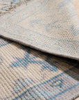 Iris Bianca Gray Hand Knotted Wool Rug, featuring subtle ivory patterns against a soft gray background, complements a light-filled room with minimalist furniture.