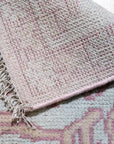 Lydia Oriental Pink Hand Knotted Wool Rug, a plush wool rug with intricate floral patterns in varying shades of pink, cream, and muted blues, lays centered on a light hardwood floor, providing a soft, luxurious accent to the room's interior.