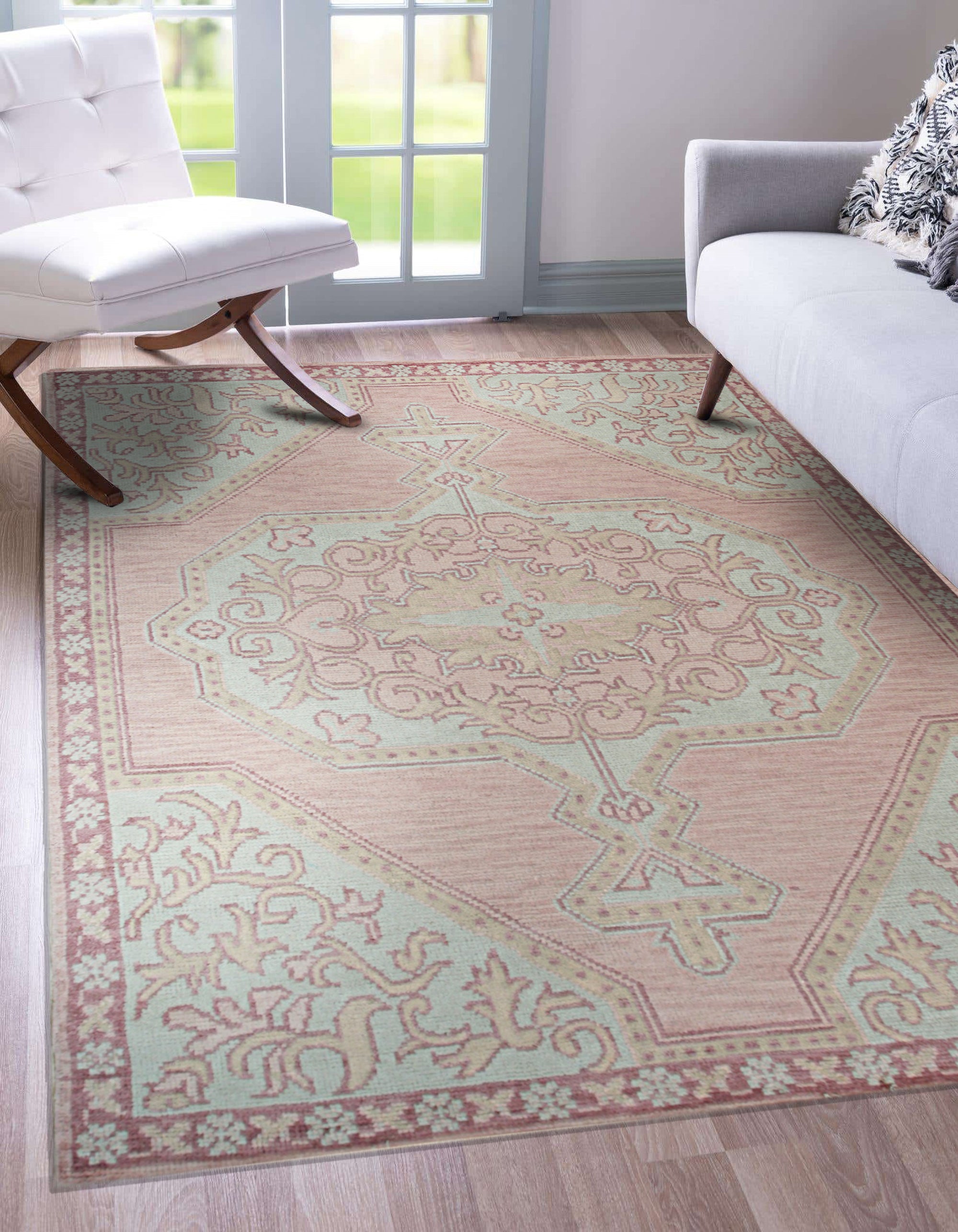 Lydia Oriental Pink Hand Knotted Wool Rug, displaying intricate patterns in warm pinks and muted neutrals, lays gracefully in a bright, modern living room, adding a touch of timeless elegance.