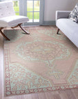 Lydia Oriental Pink Hand Knotted Wool Rug, displaying intricate patterns in warm pinks and muted neutrals, lays gracefully in a bright, modern living room, adding a touch of timeless elegance.