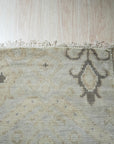Lush Traditional Gray Hand Knotted Wool Rug, its intricate floral and geometric patterns unfolding across a soft gray field, rests subtly in a warmly lit room with hardwood flooring.