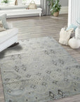 Lush Traditional Gray Hand Knotted Wool Rug, presenting intricate patterns in muted gray tones, rests on a light hardwood floor under warm, ambient lighting. The hand-knotted wool construction is evident in the detailed texture and subtle sheen.
