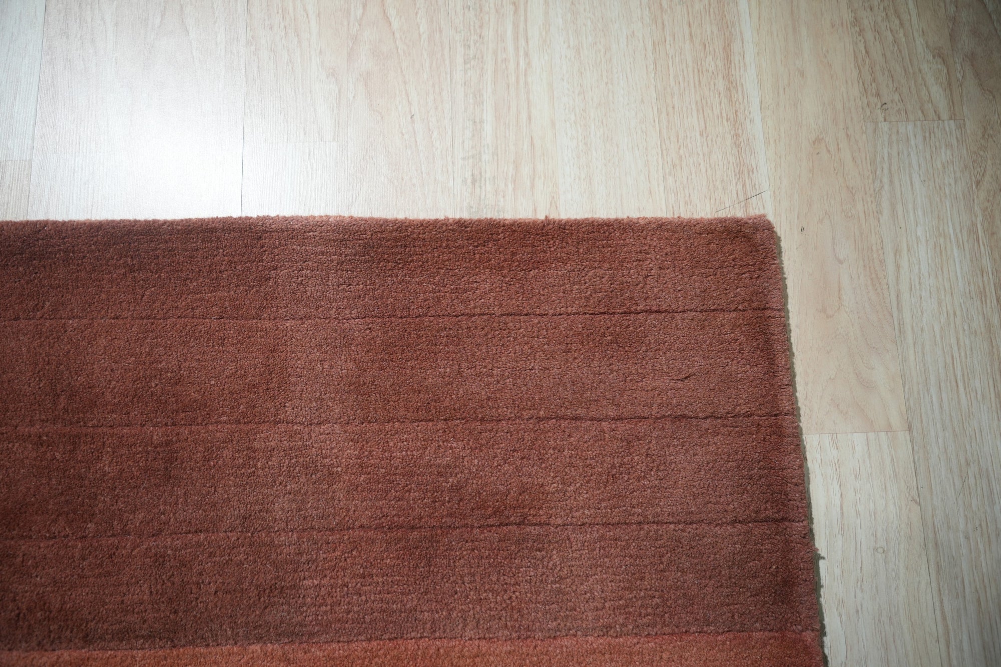 Isla Striped Rust Hand Tufted Wool Rug displayed in a bright, airy living room setting. Warm rust and cream stripes alternate across the hand-tufted wool rug, anchoring a seating area with a modern sofa and complementary decor.