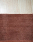 Isla Striped Rust Hand Tufted Wool Rug displayed in a bright, airy living room setting. Warm rust and cream stripes alternate across the hand-tufted wool rug, anchoring a seating area with a modern sofa and complementary decor.