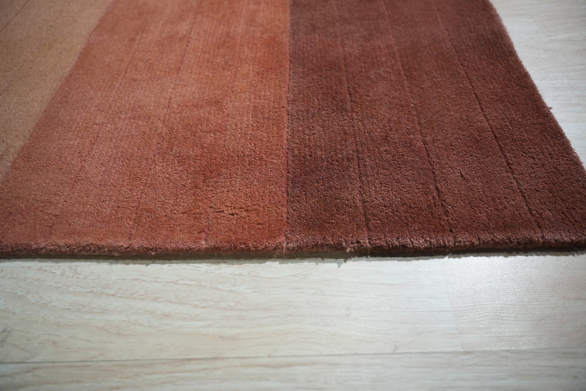 Isla Striped Rust Hand Tufted Wool Rug displayed on a polished wood floor, showcasing its warm rust tones and bold stripe design within a contemporary living space.